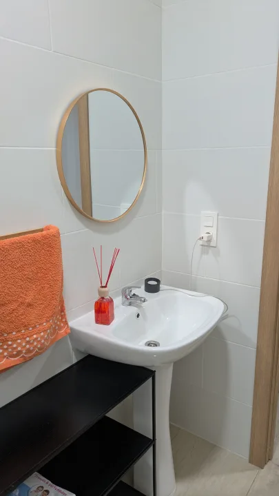 Aseo con lavabo, espejo redondo y estantería auxiliar.