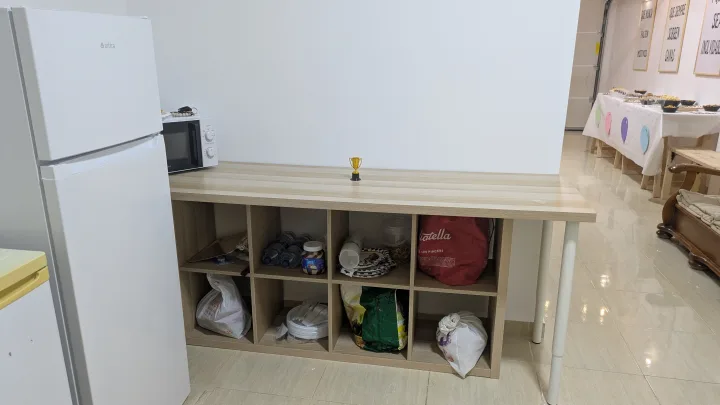 Encimera auxiliar de madera con estantes junto al frigorífico y el microondas del local.